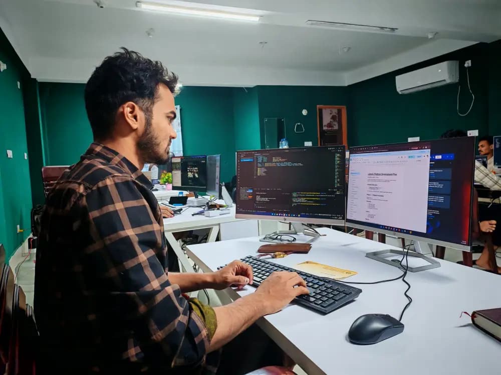 A software developer writing code at a desk with two monitors