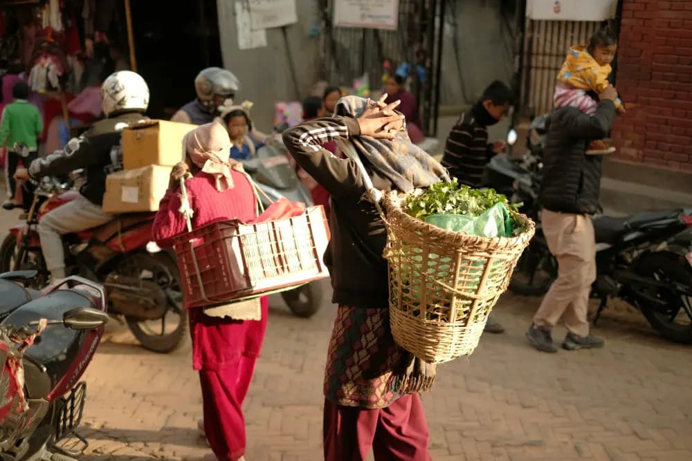 People carrying baskets and boxes past motorbikes on a Kathmandu street in the morning